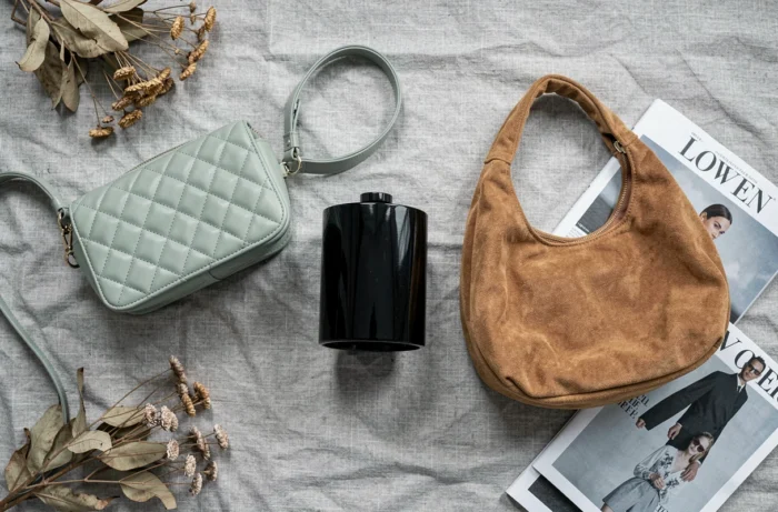 Flatlay de trois sacs à main tendance 2024 — crossbody matelassé vert sauge, pochette cylindrique noire et hobo bag en daim camel — sur fond de lin texturé